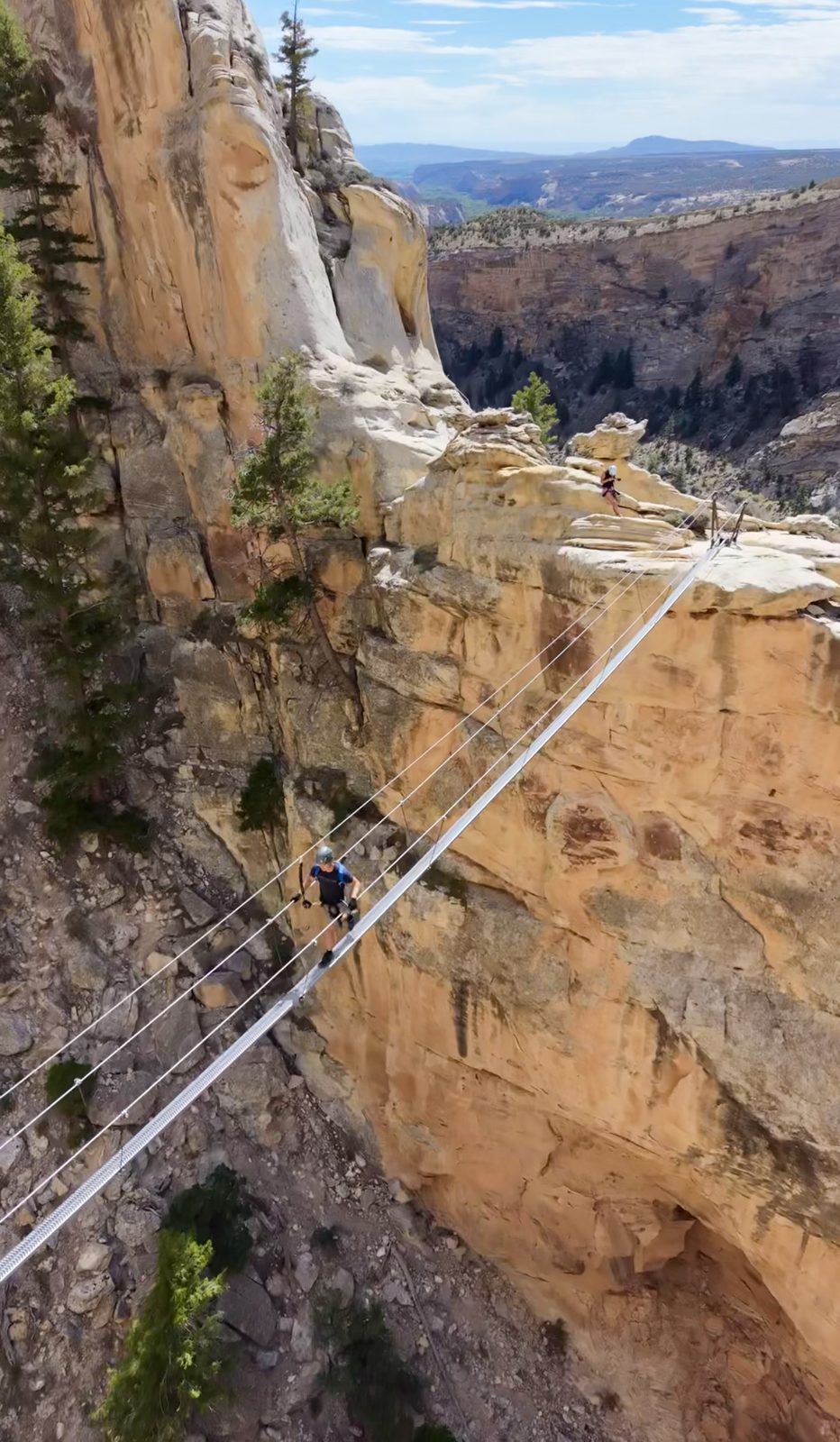 A climber crossing a cable bridge over Ashley Gorge