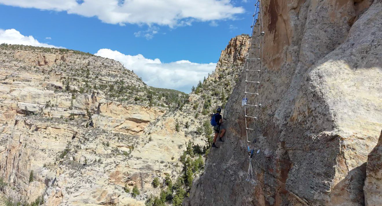 A climber on a cable ladder high above Ashley Gorge